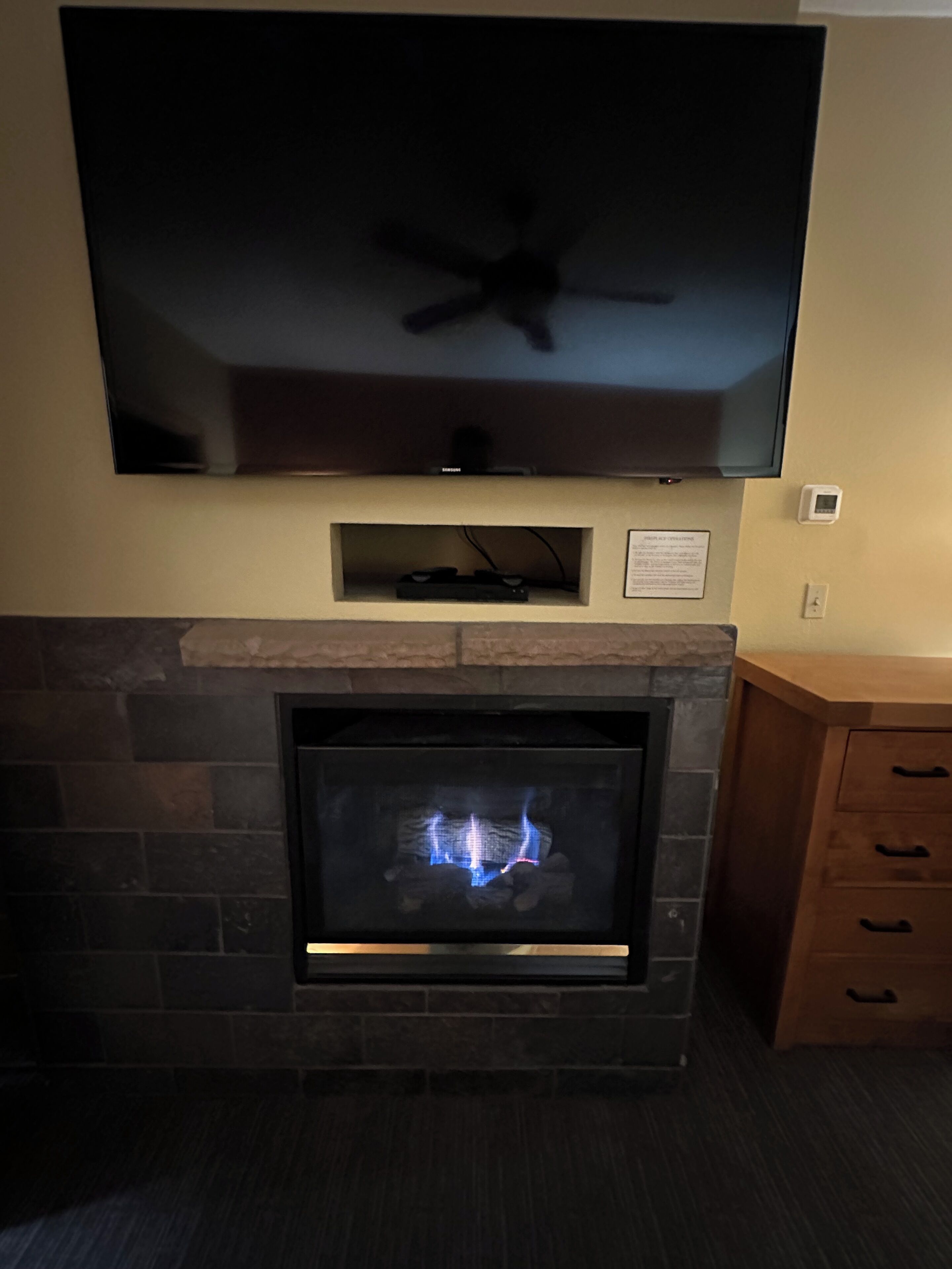 A fireplace with a TV above it, a thermostat on the wall, and a wooden cabinet to the right.
