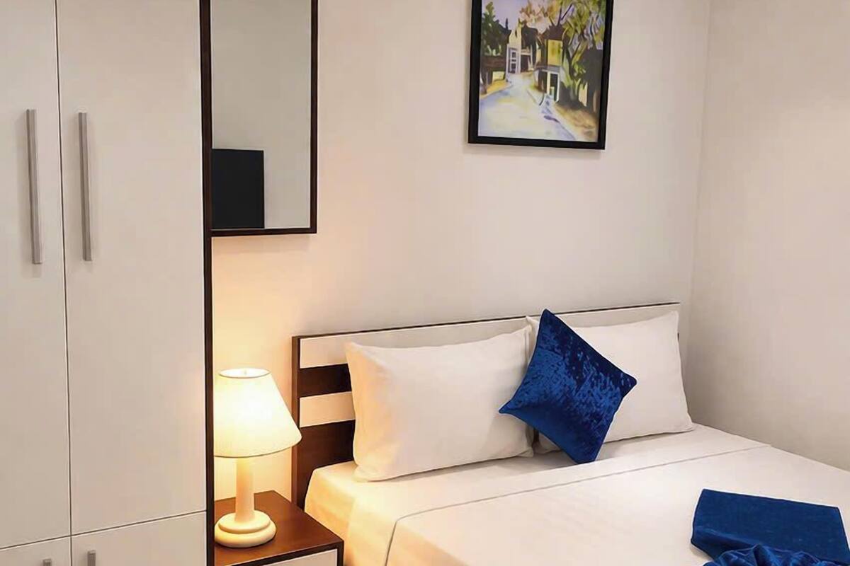 A hotel room with a bed, a nightstand, a lamp, a wardrobe, and a framed picture on the wall.