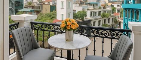 Un balcón con dos sillas, una mesa y un jarrón de flores.
