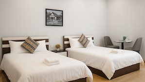 Ett hotellrum med två sängar, ett litet bord, en stol och en inramad tavla på väggen.