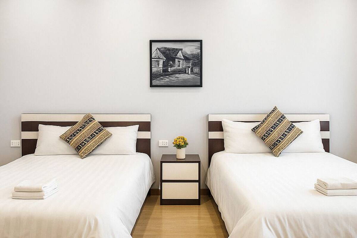 A hotel room with two beds, a nightstand with a vase of flowers, and a framed picture on the wall.