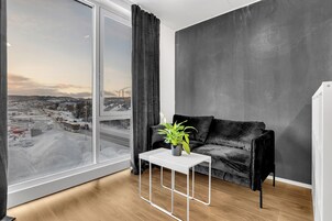 Una sala de estar moderna con un sofá negro, una mesa de centro blanca y un amplio ventanal con vistas a la ciudad.
