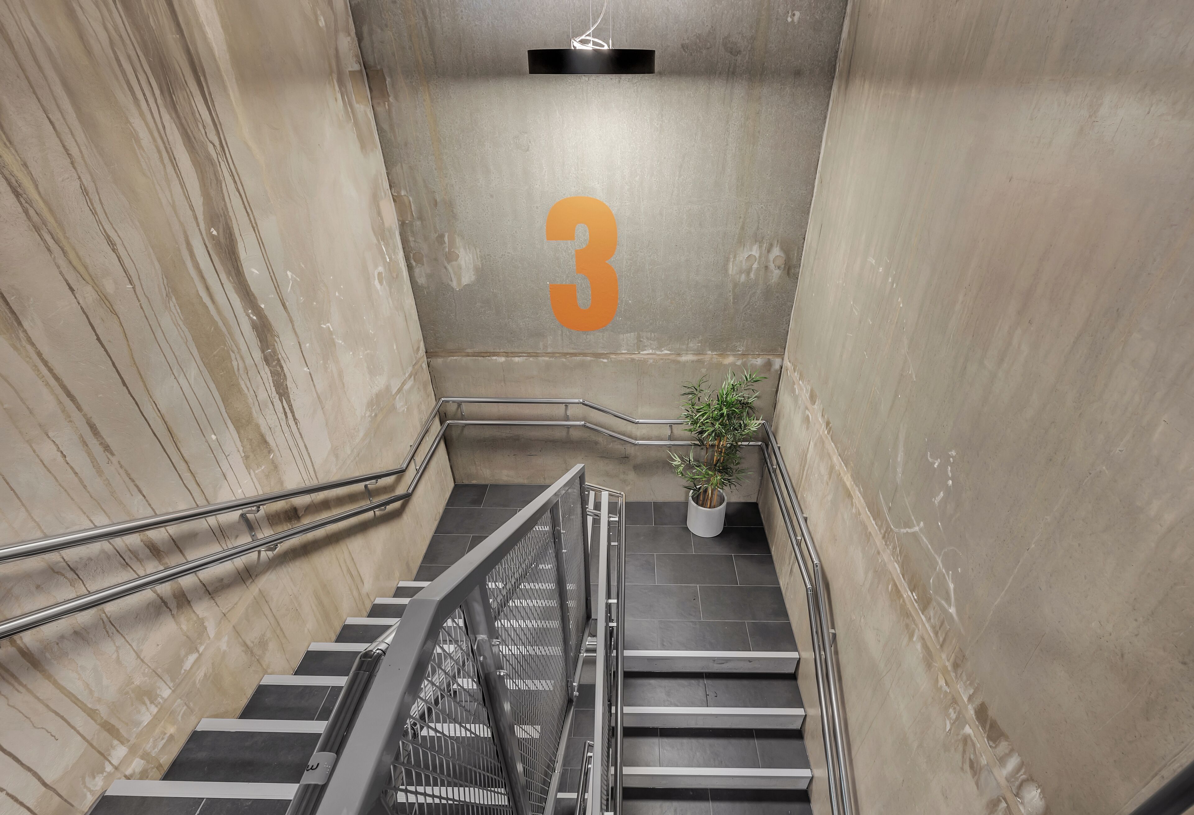 Eine Treppe mit der Zahl 3 an der Wand, Metallhandläufen und einem Blumentopf.