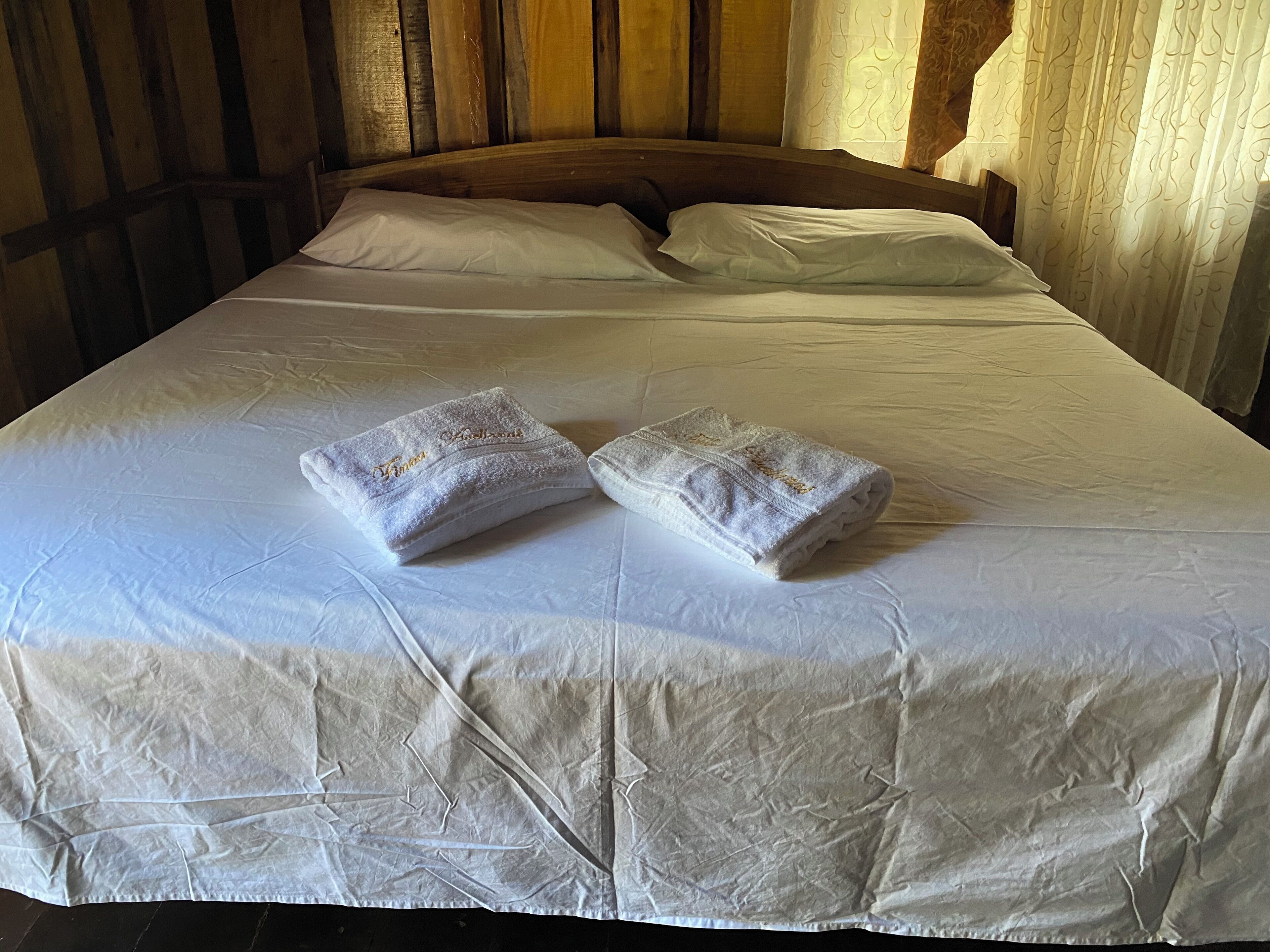 A bed with a white duvet and two towels with embroidered text.