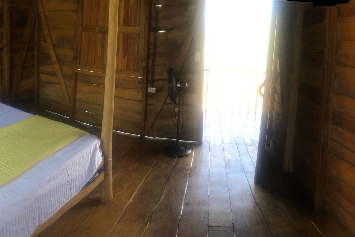 A wooden room with a bed, a chair, and a window.