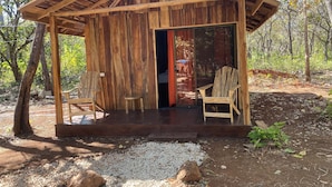 A rustic wooden cabin with a porch, two wooden chairs, and a gravel path leading to the entrance. - Finca Avellanas  (Tamarindo)