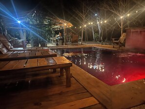 Una terrazza in legno con poltrone relax e piscina illuminata di notte.