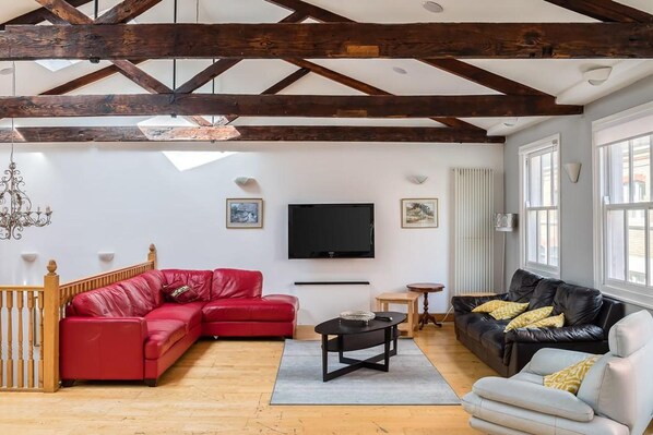A spacious living room with exposed wooden beams, a red leather sofa, a black leather sofa, a white sofa, a television, and a chandelier. - Specious Family Kensington 5-bed House, Sleeps 10 (London)