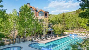 A modern building with a pool area, surrounded by trees and a hilly landscape. - Highlands Lodge 401 - 3 Bedroom Residence (Beaver Creek)