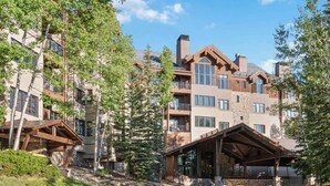 A multi-story hotel with a covered outdoor area, surrounded by trees and a clear sky. - Highlands Lodge 401 - 3 Bedroom Residence (Beaver Creek)