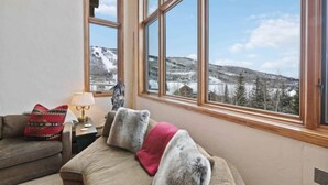 A cozy room with a sofa, a lamp, and large windows offering a view of a snowy landscape. - Highlands Lodge 401 - 3 Bedroom Residence (Beaver Creek)