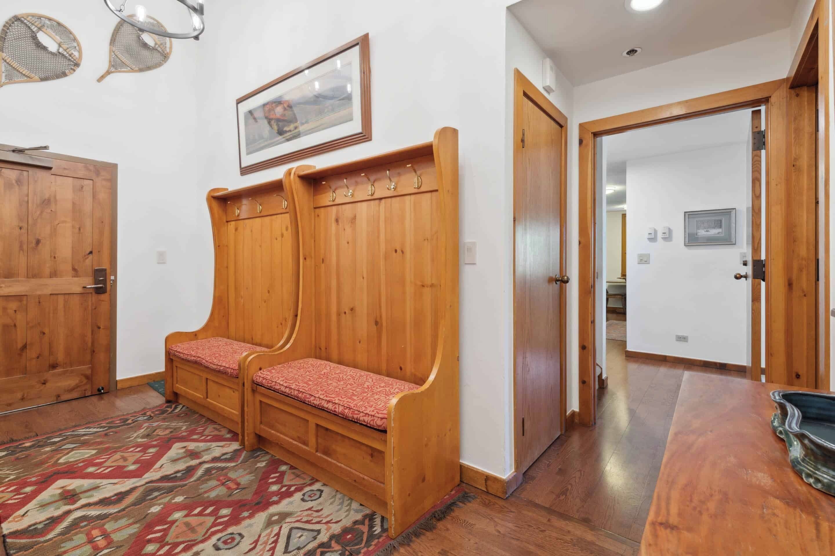 A wooden bench with a red cushion in a hallway with wooden doors and a patterned rug.