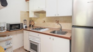 Eine kompakte Küche mit Gaskochfeld, Mikrowelle, Spüle und einem Edelstahl-Kühlschrank.