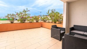Un espacio al aire libre techado con suelo de baldosas, muebles de mimbre y plantas en macetas.