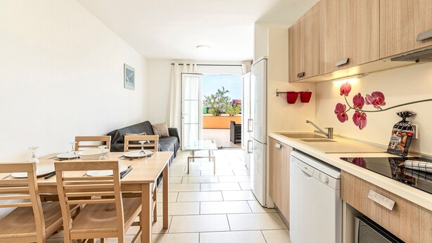 Una cocina moderna con armarios de madera, lavavajillas y un comedor con mesa y sillas.