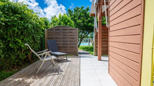 A wooden deck with a bench and a covered area, leading to a pool. - Villa Muscade - Maison avec piscine partagée (Saint-Francois)