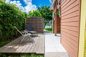 Une terrasse en bois avec un banc et un espace abrité, donnant accès à une piscine.