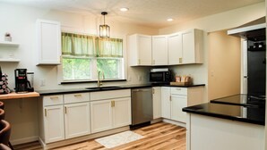 A modern kitchen with white cabinets, a stainless steel dishwasher, a black microwave, and a black refrigerator.