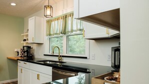 A modern kitchen with white cabinets, a black countertop, and a window with curtains.