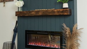 A modern living room with a dark blue wall, a flat-screen TV mounted above a fireplace, and a wooden shelf with decorative items.