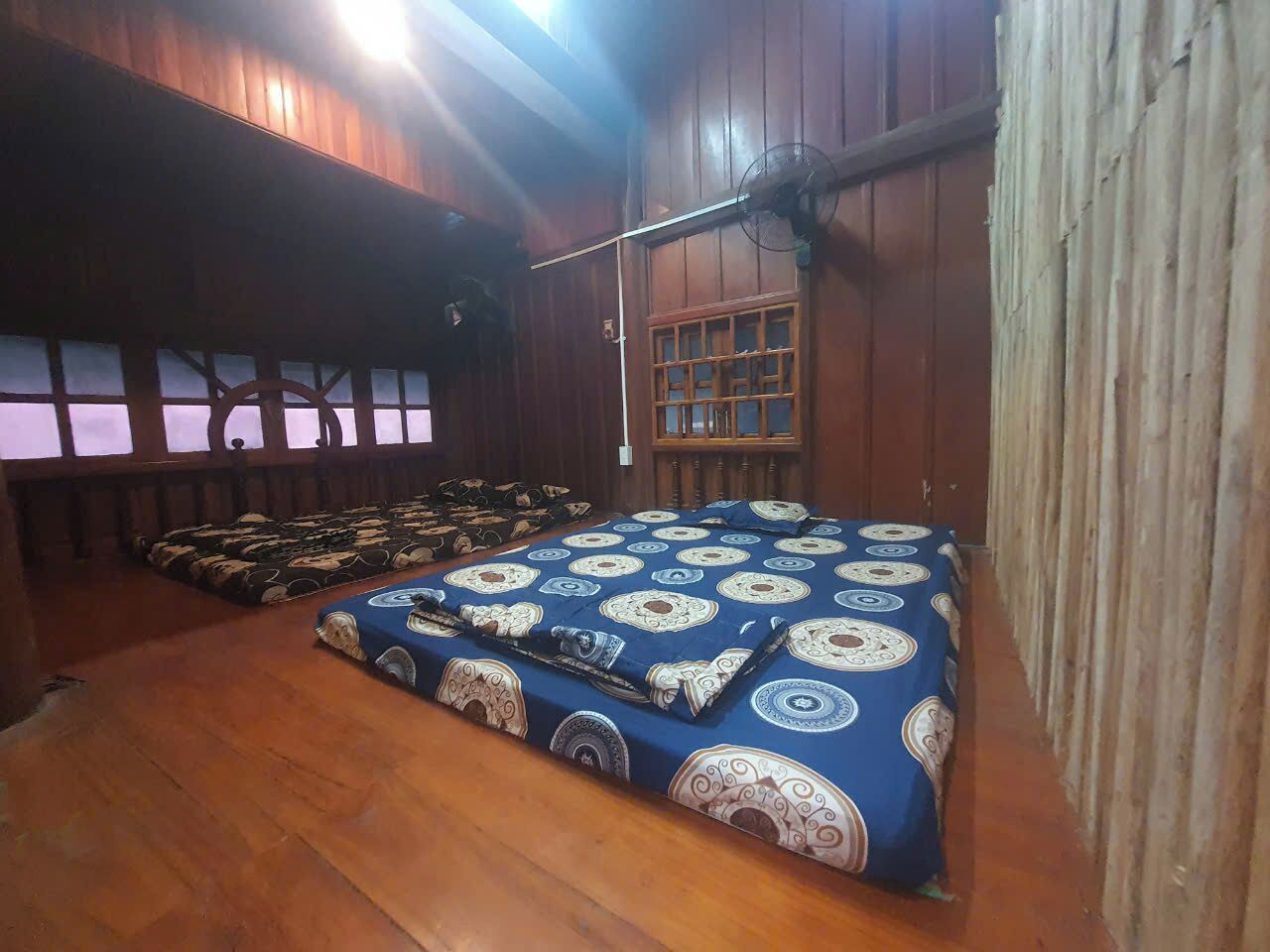 A room with a large bed, a fan, and a window with a grid pattern.