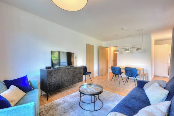 Un salon moderne avec un canapé, une table basse et un téléviseur posé sur un meuble. On y trouve également un coin repas avec des chaises et une table.