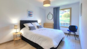 A bedroom with a bed, bedside tables, a chair, a window with curtains, and a wall-mounted mirror.