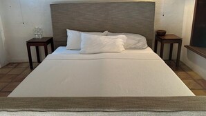 Een net opgemaakt bed met witte lakens en kussens, een houten hoofdbord en twee kleine nachtkastjes met waterflesjes erop.