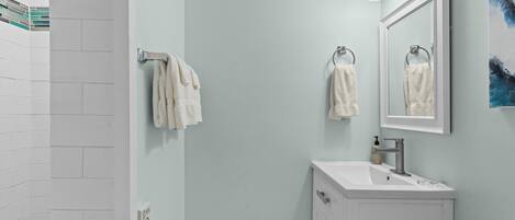 A bathroom with a white sink, a mirror, and two towels hanging on towel racks.