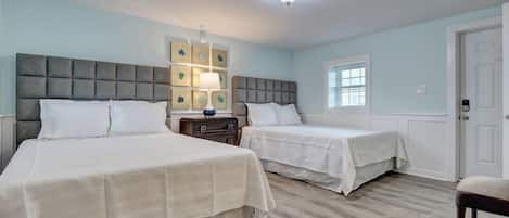 A bedroom with two beds, a nightstand, a lamp, and a window.