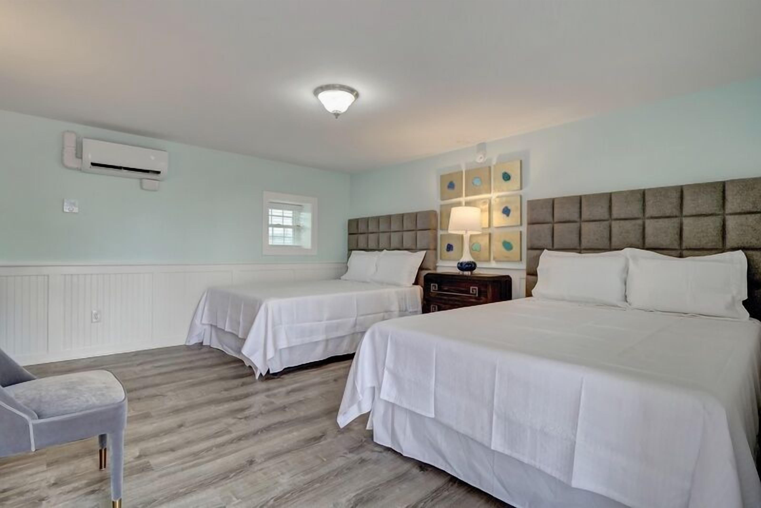 A hotel room with two beds, a chair, a nightstand, a lamp, and a window.