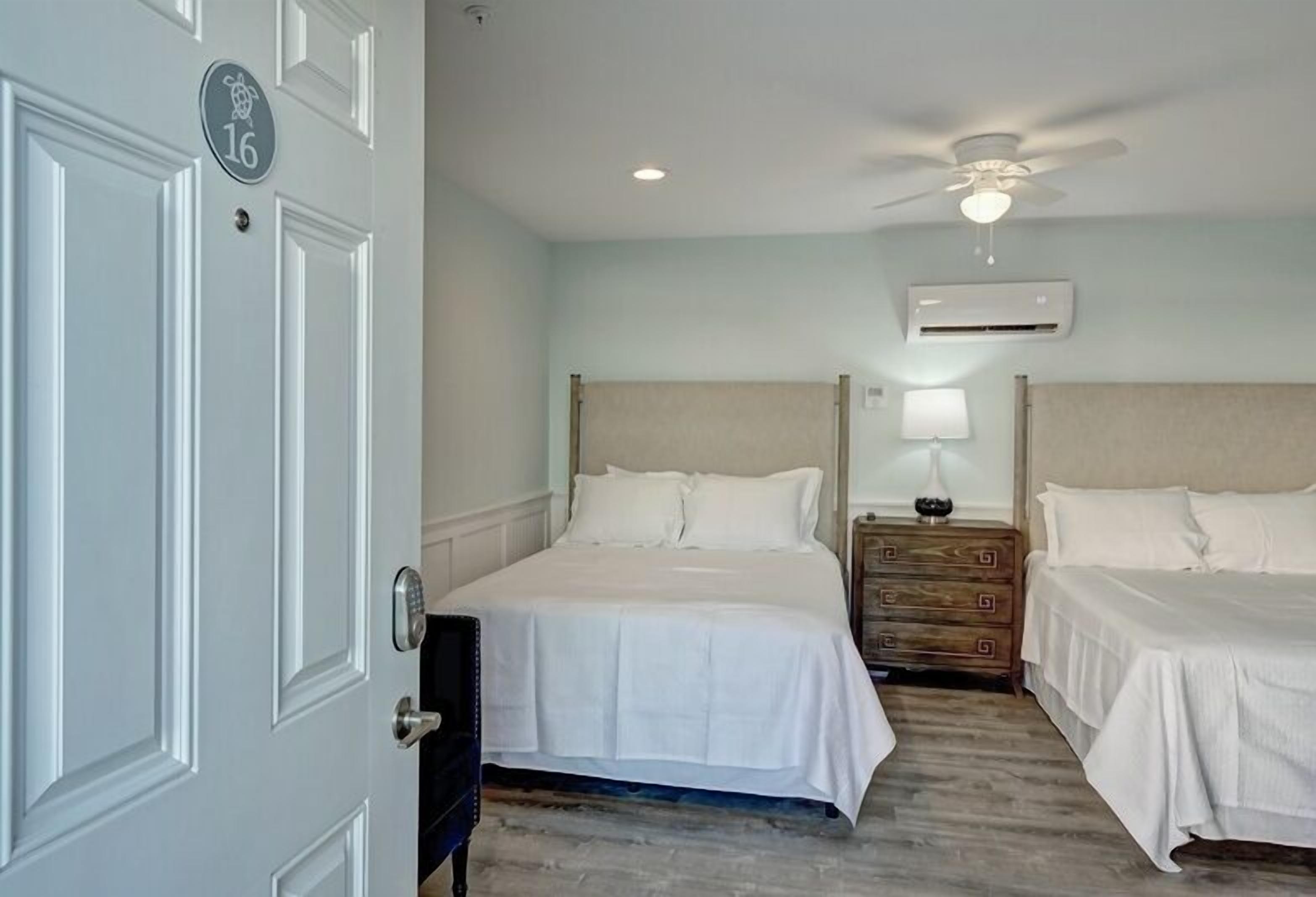 Une chambre d’hôtel avec deux lits, un ventilateur de plafond, un appareil de climatisation et une table de chevet avec une lampe.