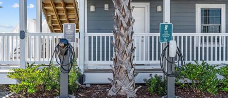 A building with a covered porch, two electric vehicle charging stations, and a palm tree.