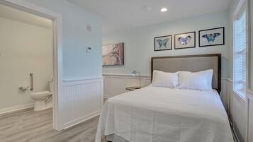 A bedroom with a bed, a nightstand, a wall-mounted lamp, and a window with blinds.
