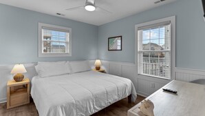Una camera da letto con un letto, due comodini con lampade, una ventola a soffitto e due finestre con persiane.