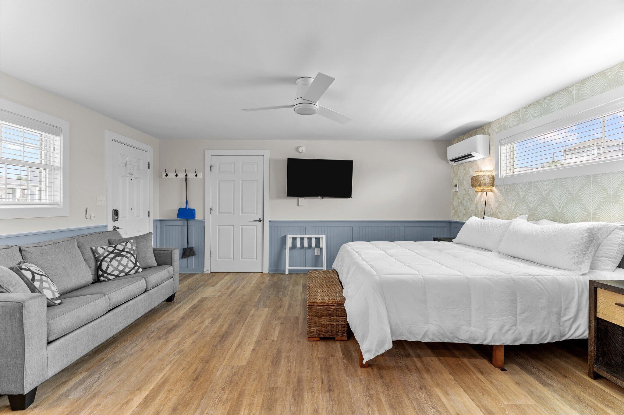 A bedroom with a bed, a sofa, a ceiling fan, a TV, and a window.