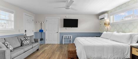 A bedroom with a bed, a sofa, a ceiling fan, a TV, and a window.