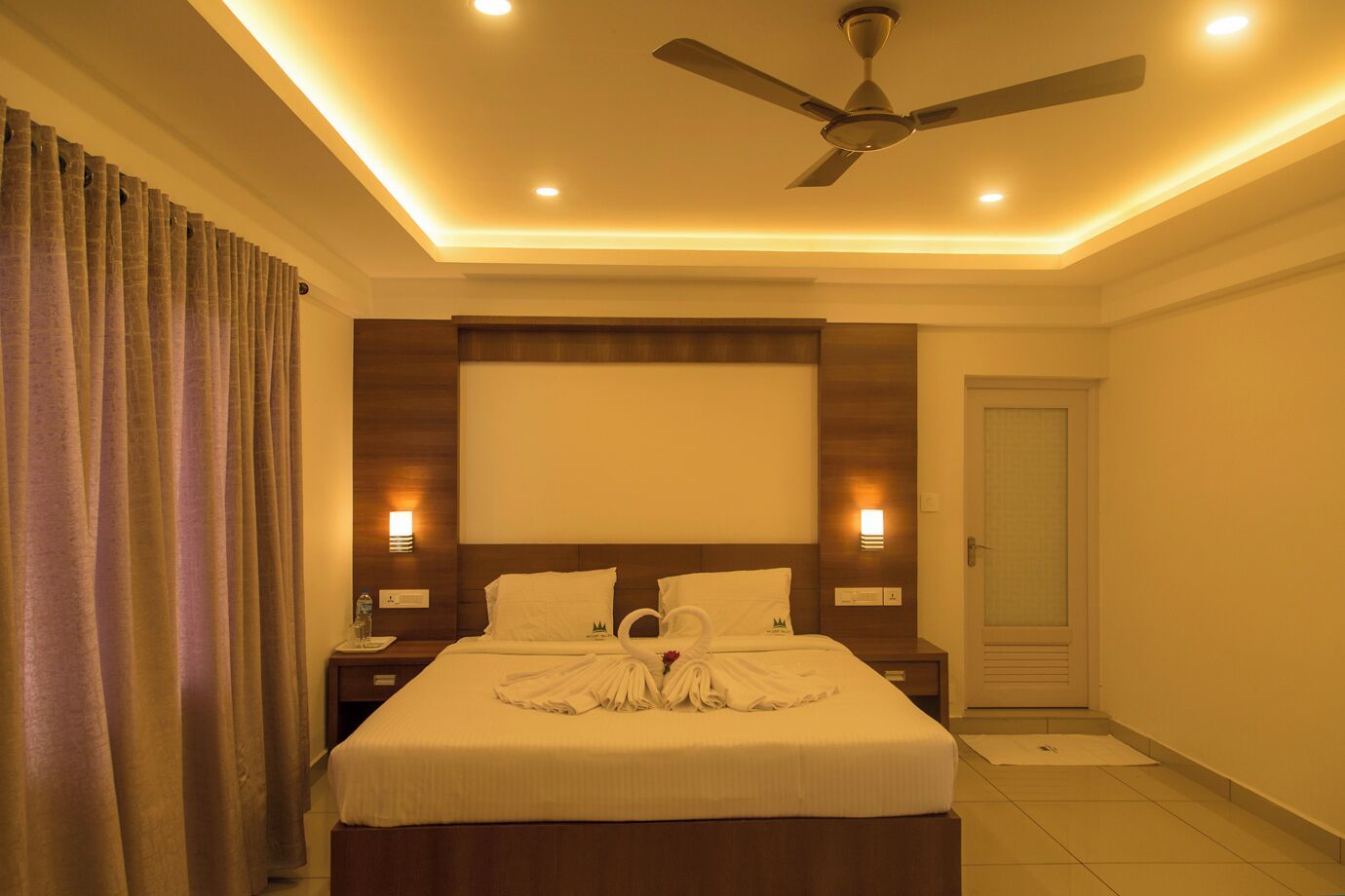 A hotel room with a bed, a ceiling fan, and two bedside lamps.