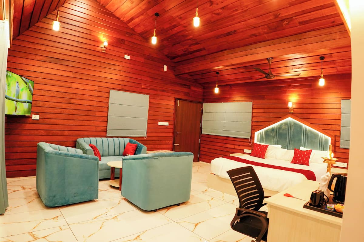 A hotel room with a wooden ceiling, a bed with a white headboard, a blue sofa, a small table, and a chair.
