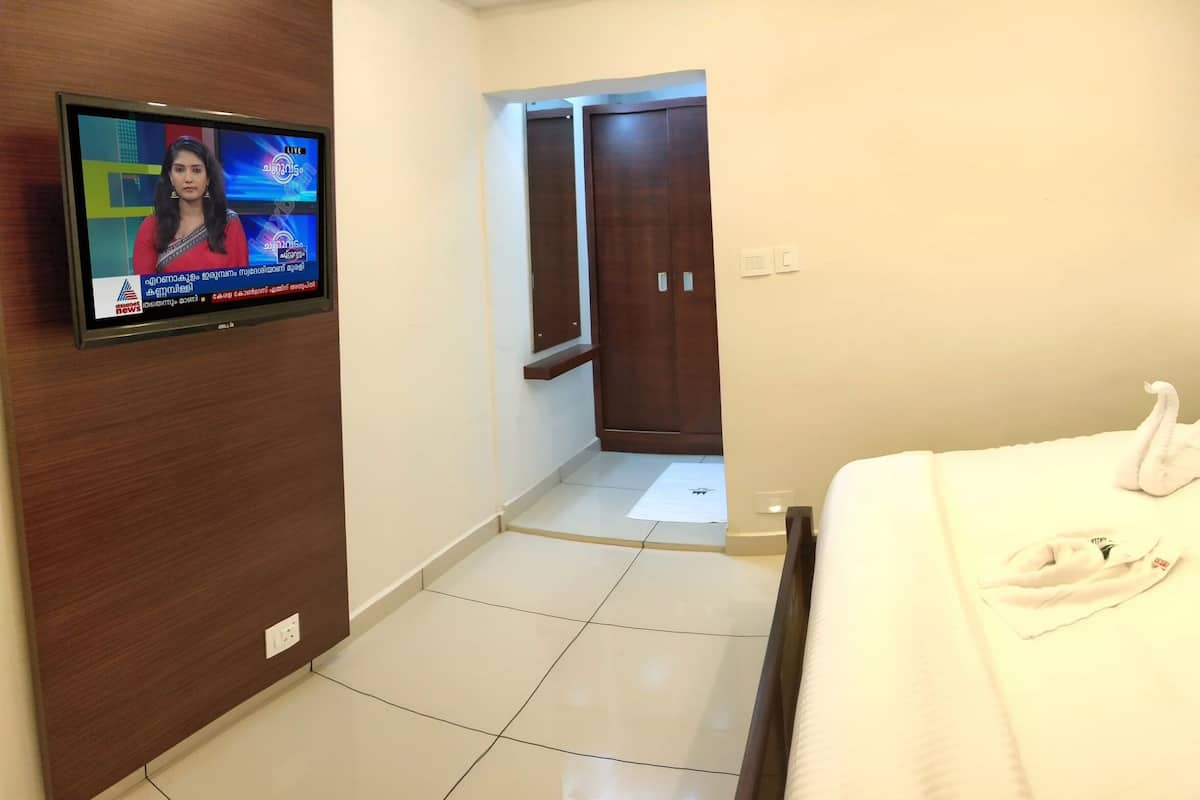 A hotel room with a bed, a TV mounted on the wall, a wooden wardrobe, and a nightstand with a phone.