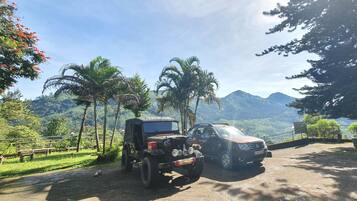 Un jeep y un coche estacionados en una zona pavimentada, con una vista panorámica de montañas y palmeras al fondo.