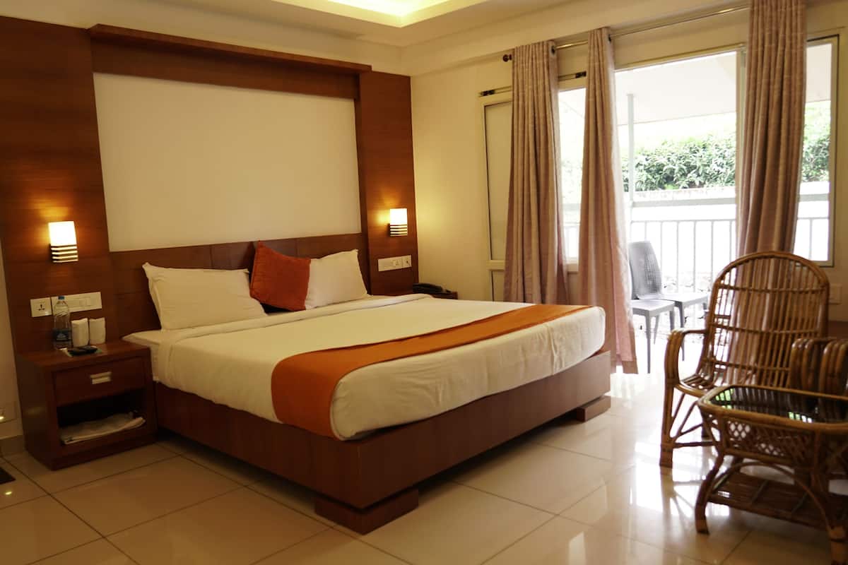 A hotel room with a large bed, wooden headboard, bedside tables, a chair, and a balcony with curtains.
