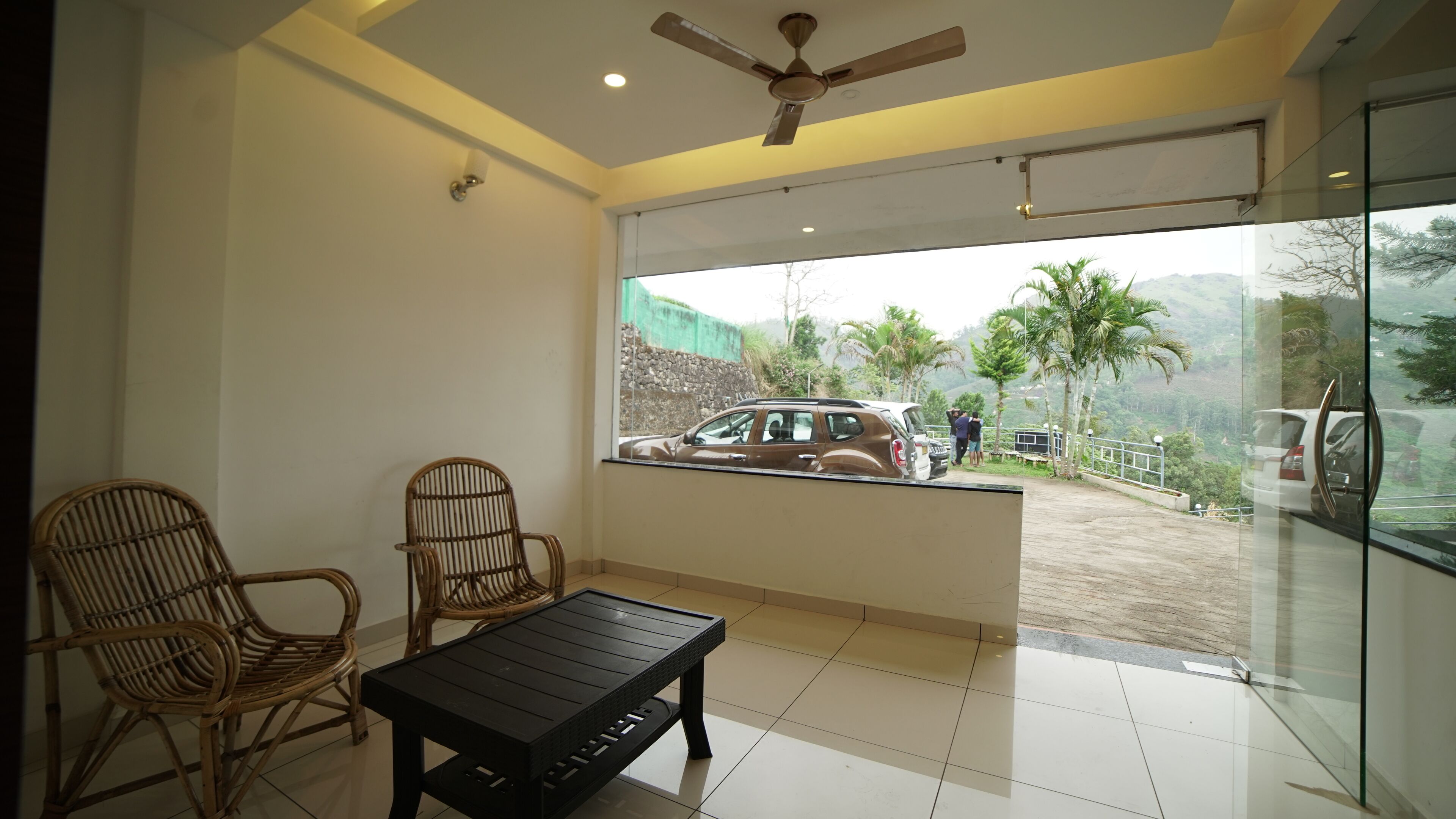 A room with a ceiling fan, a glass door leading outside, and a view of a car and people outside.