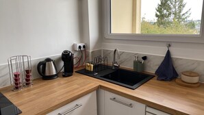 A modern kitchen with a wooden countertop, a black sink, and a window with a view of trees. - "Bellevue - 35 m2 - parking - 10 min downtown - Normandy - Saint Lô (Saint-Lô)