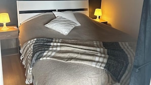 A neatly made bed with a white headboard, a grey blanket, and a striped throw. There are two bedside lamps with yellow shades. - "Bellevue - 35 m2 - parking - 10 min downtown - Normandy - Saint Lô (Saint-Lô)