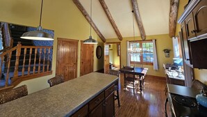 A spacious kitchen with wooden beams, a central island, and a dining area with a staircase leading to a second floor.