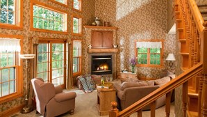 A cozy living room with a fireplace, wooden furniture, and large windows.