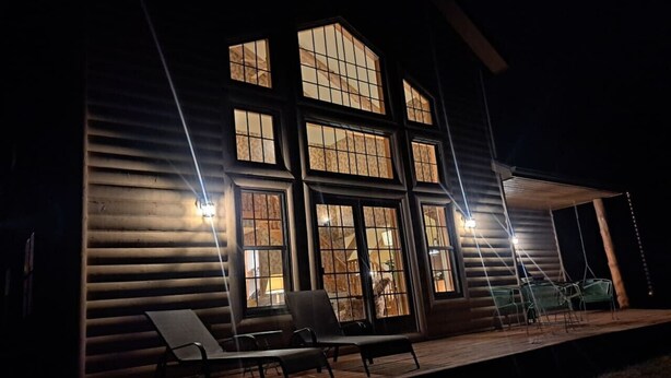 A log cabin with large windows, a covered porch with chairs, and a small outdoor seating area.
