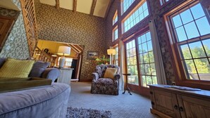A spacious living room with a high ceiling, large windows, and a staircase leading to another level.