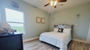 Een slaapkamer met een bed, een plafondventilator, een dressoir en een raam met uitzicht op de omgeving.